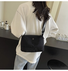 Detailed view of the adjustable shoulder strap and metal M logo on black nylon crossbody bag