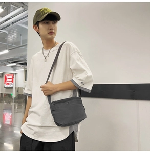 Detail of dark grey canvas crossbody bag with metal buckle and adjustable strap on model
