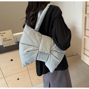 Side view of a light blue bow-shaped puffy shoulder bag on a model in a modern room