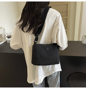 Detail of black nylon crossbody bag featuring a round metal M logo and adjustable wide strap
