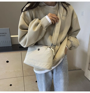 Detail of a minimalist beige nylon crossbody bag worn by a model in casual wear