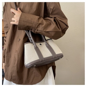 Detail of canvas tote bag with leather straps worn by model against a neutral background