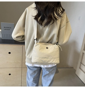 Detail of beige nylon crossbody bag with wide shoulder strap worn by a model