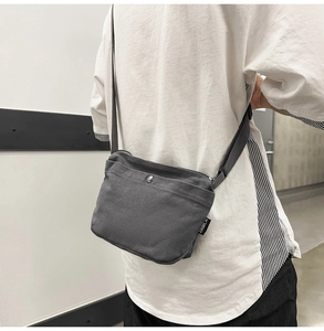Detailed close-up of a grey canvas crossbody bag showing metal snap and woven label