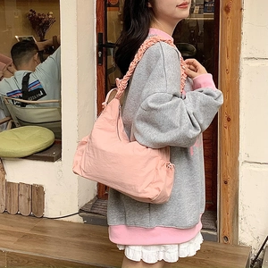 Pink nylon hobo bag with ruffled shoulder strap shown on model in street setting