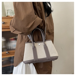 Detail of canvas and grey leather tote bag showing metal feet and round handles on a model