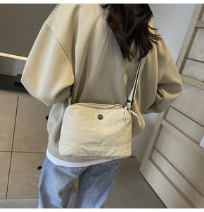 Detail view of a beige nylon crossbody bag with multi-zipper layers on a female model