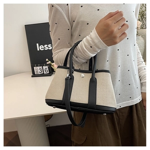 Detailed close-up of a minimalist beige canvas tote with black leather trim and silver clasp