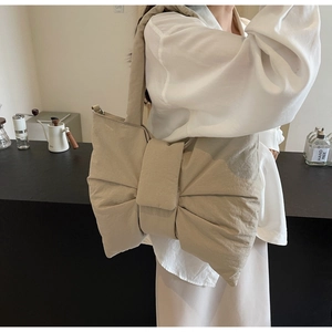 Detail of a beige bow-shaped tote bag with pleated texture worn on a shoulder