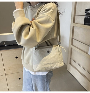 Beige nylon crossbody bag with wide shoulder strap shown in a minimalist setting