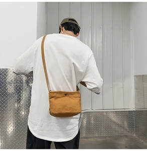 Rear view of a minimalist brown canvas crossbody bag with metal snap closure on a male model