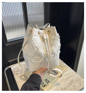 Detail of white denim bucket bag featuring quilted fringe texture and drawstring closure