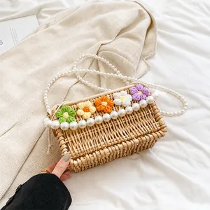 Detail of woven straw crossbody bag with colorful crochet flowers and pearl strap