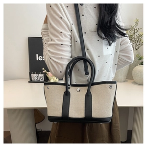 Detail of a beige canvas tote bag with black leather trim and crossbody strap on a model