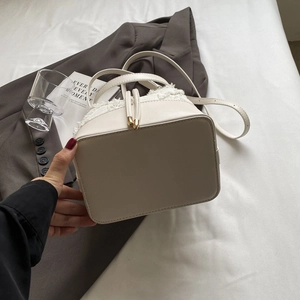 Detail of cream white bucket bag with tweed texture and drawstring closure on grey suit