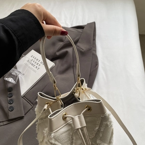 Detail of white quilted denim bucket bag with gold hardware and drawstring on gray background