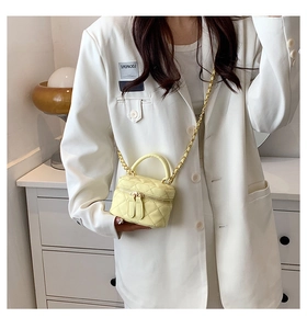 Detail of a bright yellow quilted mini bag with gold chain strap and dual zippers