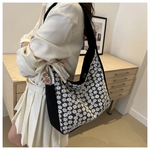 Close-up of intricate white daisy lace embroidery and pink rose bow on black canvas bag