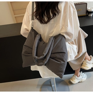 Detailed view of dark grey oversized bow-shaped tote bag worn by a model in a modern room