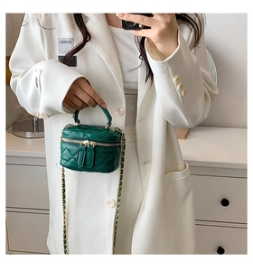 Detail of dark green quilted mini box bag with gold chain strap on model in home setting