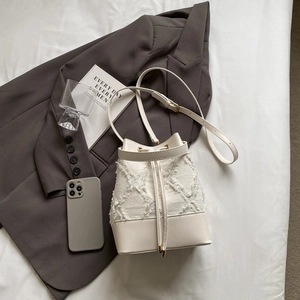 Close-up of cream-white bucket bag featuring frayed denim diamond pattern and leather strap