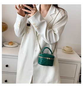 Detail view of a dark green quilted mini crossbody bag with gold chain strap and top handle