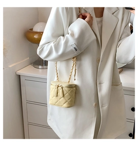 Detail of pale yellow quilted mini camera bag with gold chain strap on model