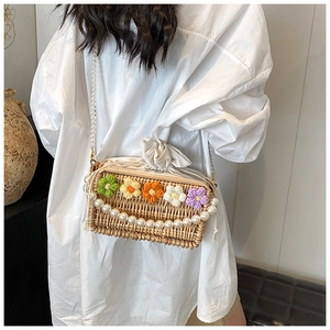 Detail view of woven straw bag with handmade crochet flowers and pearl shoulder strap