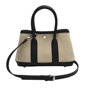 Minimalist beige canvas tote bag with black leather trim and adjustable strap in white background