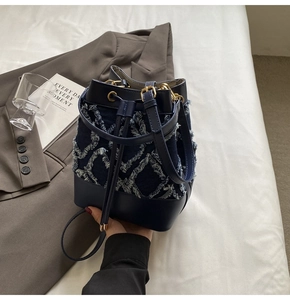 Detail of blue denim bucket bag featuring frayed diamond pattern and drawstring closure