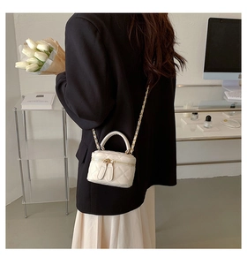 White quilted mini crossbody bag with gold chain strap shown on a female model