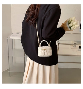 Detail of a beige quilted PU leather mini bag with gold chain strap shown on a model