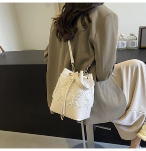 Detail view of a cream patchwork bucket bag with fringe texture and gold hardware