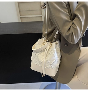Close-up of denim quilted bucket bag featuring leather base and gold-tone hardware detail