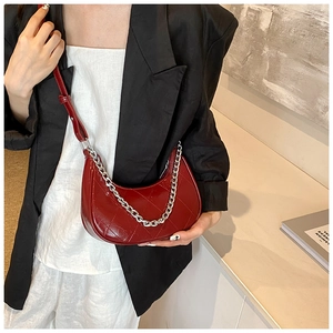 Détail du sac demi-lune bordeaux matelassé avec chaîne argentée porté sur un blazer noir