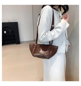 Detail view of retro brown faux crocodile leather tote bag worn by a model in a studio