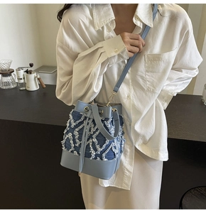 Detail of light blue denim bucket bag featuring white fringe diamond patterns and drawstrings