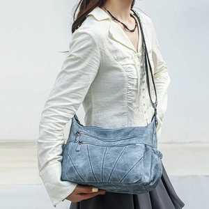 Detail of light blue PU leather crossbody bag with metal zippers and white stitching