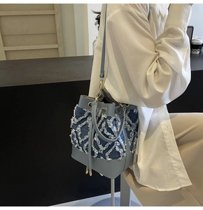 Detailed shot of denim bucket bag with white fringed diamond pattern and leather strap