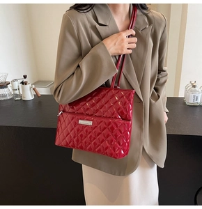 Detail of a deep red glossy quilted tote bag with silver zipper and metallic logo