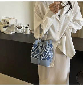 Detail of light blue denim bucket bag featuring white fringe diamond patterns and gold hardware