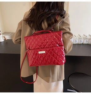 Macro detail of red quilted patent leather backpack with polished metal logo plaque