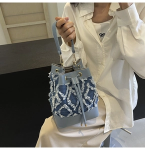 Detail view of denim bucket bag with quilted fringe textures and light blue leather handle
