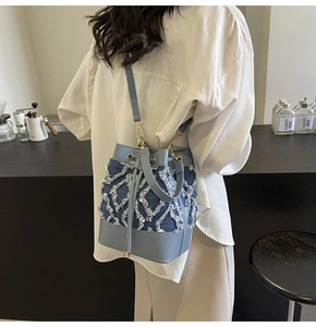 Detail of denim quilted bucket bag with light blue leather handles and gold metal hardware
