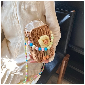 Detail of straw bucket bag with floral plush charm and colorful beaded shoulder strap