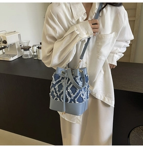 Close-up of distressed denim quilted bucket bag with light blue leather strap and gold hardware