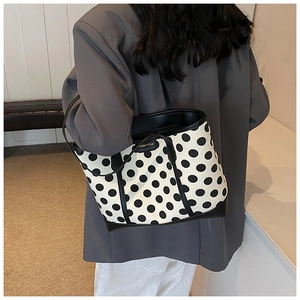Detailed view of black and white polka dot tote bag with premium leather trim and gold tag