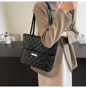 Detail of black quilted tote bag featuring glossy PU leather and a metallic brand plaque