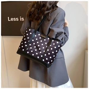Detail of a chic polka dot tote bag with black leather trim and gold logo on a model