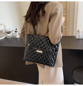 Close-up of black quilted leather tote bag with silver logo and zipper detail
